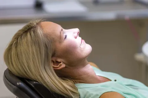 Woman relaxing in dental chair with light shining on her face during a dental appointment.