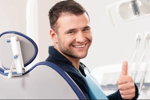 Smiling man giving a thumbs-up in a dental chair, showing positivity and confidence during a dental visit.