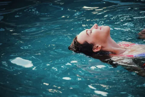 Woman relaxing and floating peacefully on her back in a clear blue swimming pool.