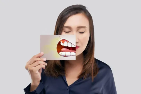 A woman holds a card featuring a cartoon mouth, expressing emotions. Gray background.