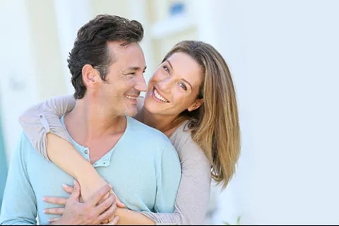Smiling woman embraces happy man from behind in a bright, airy setting, expressing love and affection.