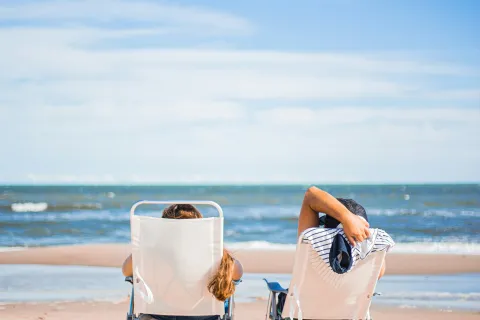 Couple relaxing on beach chairs facing the ocean under a clear blue sky on a sunny day