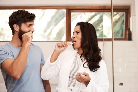 Couple brushing their teeth in a bright bathroom, smiling and enjoying their morning routine together.