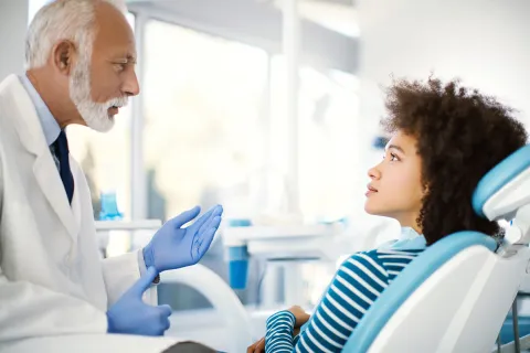 A dentist consults a young woman in a bright dental clinic, discussing treatment options.