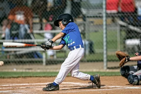 Young baseball player in blue batting during a game with catcher and ball in view on a sunny day.