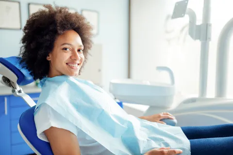 Smiling woman sitting in a dental chair with a dental bib in a bright clinic.