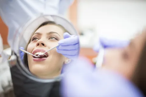 Dentist examining a woman's teeth using a mirror and tools in a clinical setting.