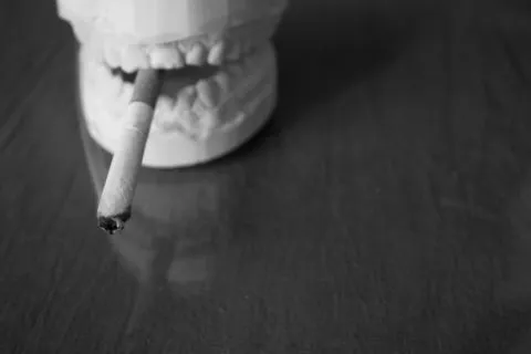 A skull sculpture with a cigarette held in its open mouth on a dark table.