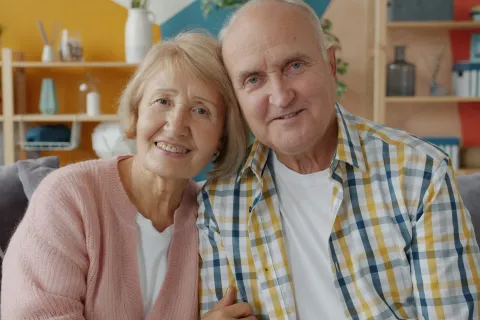 Smiling elderly couple sitting close together on a couch in a cozy, modern living room.