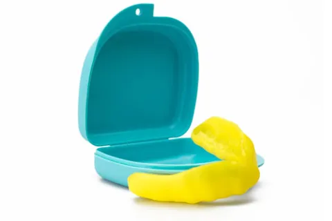 Bright yellow mouthguard next to an open turquoise protective case on a white background.