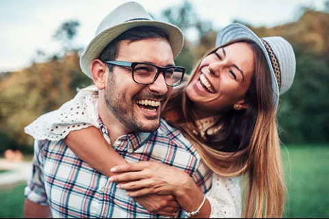 Happy young couple wearing hats laughing outdoors in a park on a sunny day
