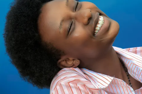 Smiling woman with curly hair in striped shirt against bright blue background, expressing joy with closed eyes.