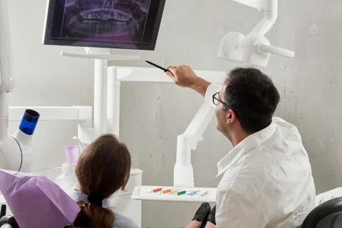 Dentist showing patient a dental X-ray on a screen during a consultation in a modern dental clinic.