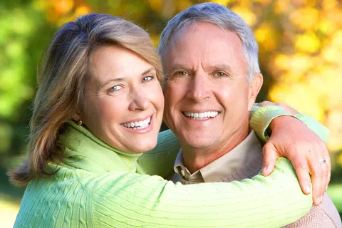 Smiling mature couple embracing outdoors with autumn foliage in the background