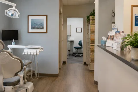 Modern dental office with treatment chair, dental equipment, and reception area featuring plants and brochures.