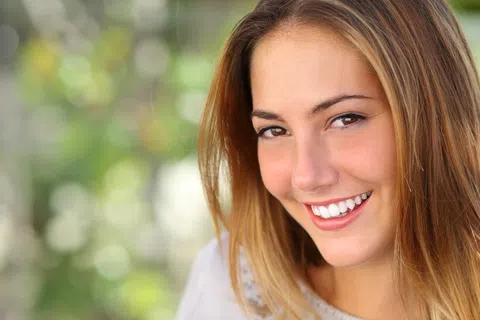 Close-up of a smiling young woman with long light brown hair against a blurred green background