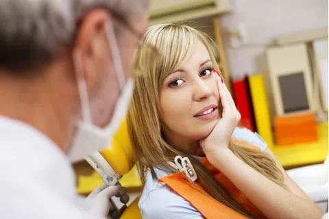 Young woman experiencing tooth pain during dental exam with dentist wearing mask and gloves