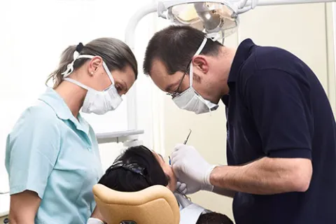 Dentist and dental assistant wearing masks treating a patient's teeth in a dental clinic chair.