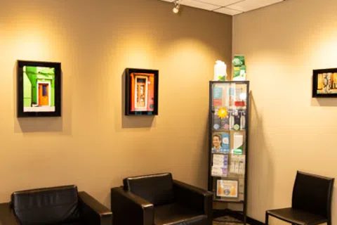 Modern waiting room with black leather chairs, informational display cabinet, and colorful framed art on beige walls.