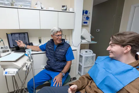 Senior male dentist explaining dental X-ray results to a young male patient in a modern dental clinic.