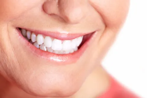 Close-up of a smiling person's mouth showing white teeth and smooth skin with a natural glow.