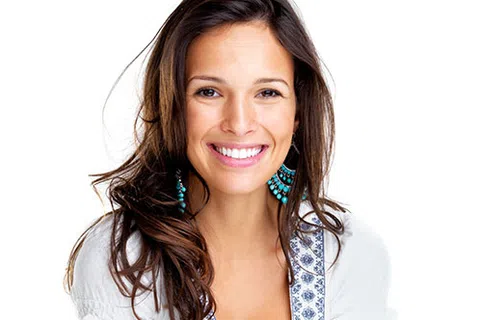 Smiling woman with long brown hair wearing turquoise earrings and a white patterned top against white background