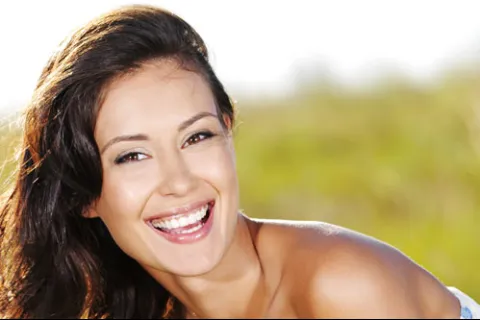 Smiling young woman with long dark hair outdoors in natural sunlight with a blurred greenery background