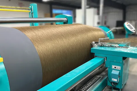 Industrial machine winding brown textile fiber in a factory setting with teal machinery components.