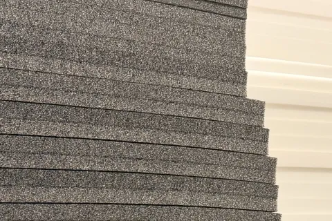 Stack of dark gray foam sheets next to white corrugated plastic sheets with linear texture