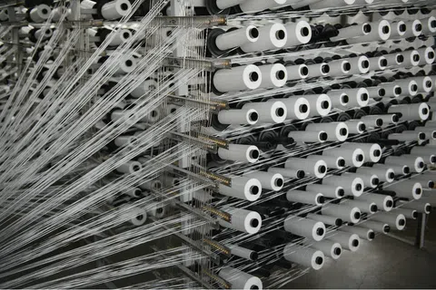 Rows of white thread spools with threads organized on a textile manufacturing machine in a factory.