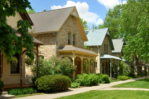 Charming neighborhood featuring traditional brick houses with lush greenery and walkways on a sunny day.