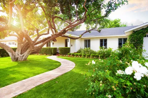 Charming white house with manicured garden and winding pathway under sunlight.