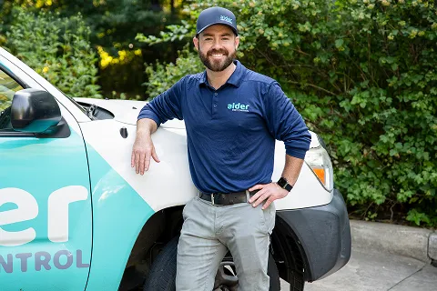 Alder Control technician poses beside a branded service vehicle in a green outdoor setting.