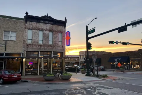 Historic downtown street corner at sunset with vintage buildings, neon signs, and traffic lights.