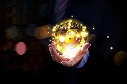 Businessman holding glowing golden shield with digital lock symbol representing cybersecurity and data protection.
