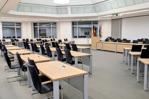 Modern empty conference room with wooden desks, black chairs, and a circular skylight ceiling.