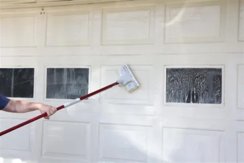a hand holding a red and white object with a white wall and a window with a white frame