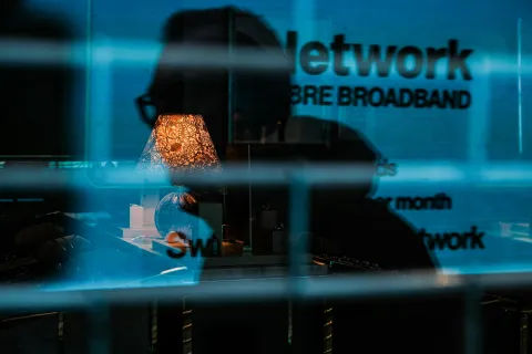 Silhouetted person behind reflective glass with illuminated lamp and network broadband text overlay