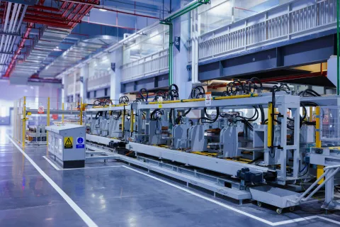 Modern automated industrial machinery line in a clean, spacious manufacturing facility with overhead piping and lighting.