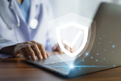 Doctor using laptop with digital shield and check mark symbol representing cybersecurity and data protection.