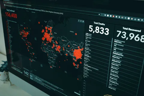 Computer screen showing global COVID-19 map with confirmed cases, total deaths, and recoveries data in red and white text.