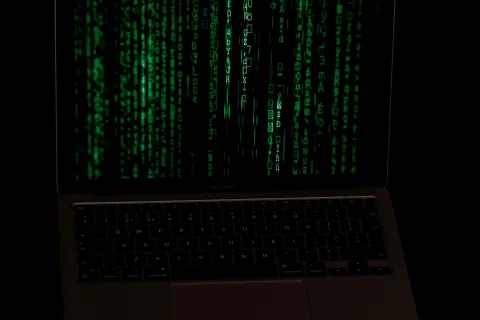 Laptop screen displaying cascading green digital code on black background representing hacking or coding.