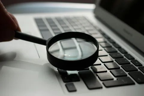 Magnifying glass held over a laptop keyboard highlighting keys in close-up view for inspection.