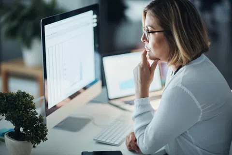 Woman in glasses analyzing data on desktop and laptop screens in a modern office environment.