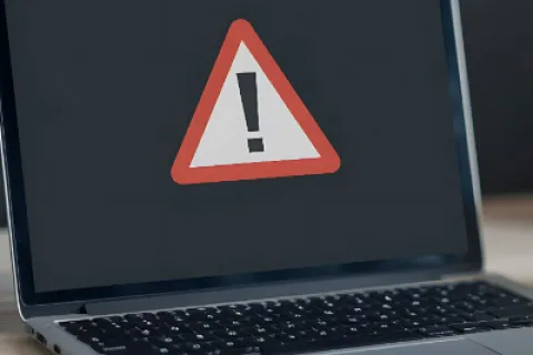 Laptop screen displaying a red triangular warning sign with an exclamation mark on a black background.