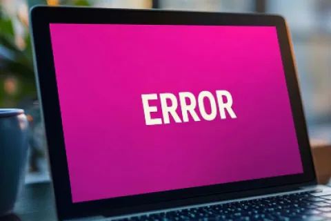 Laptop screen displaying bold white ERROR text on a bright pink background in a modern workspace.