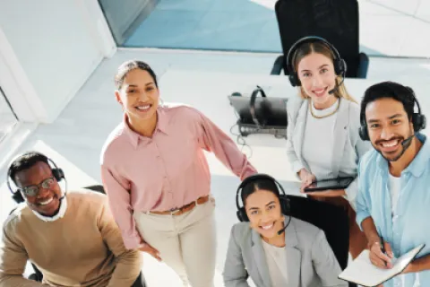 Diverse customer support team with headsets smiling and collaborating in a bright modern office environment
