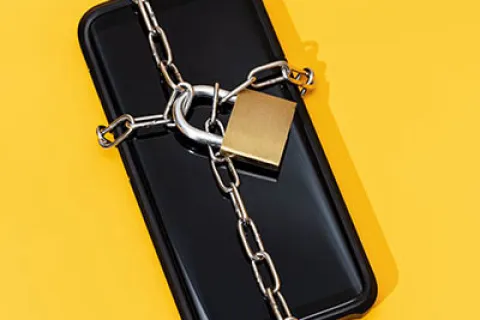 Smartphone wrapped in metal chain with padlock on bright yellow background symbolizing mobile security.