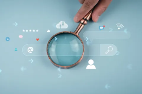 Hand holding magnifying glass over digital search bar and icons on blue background showing online search concept
