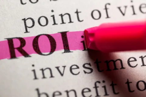 The term ROI highlighted with a pink marker on a printed page focused on investment and benefit text.